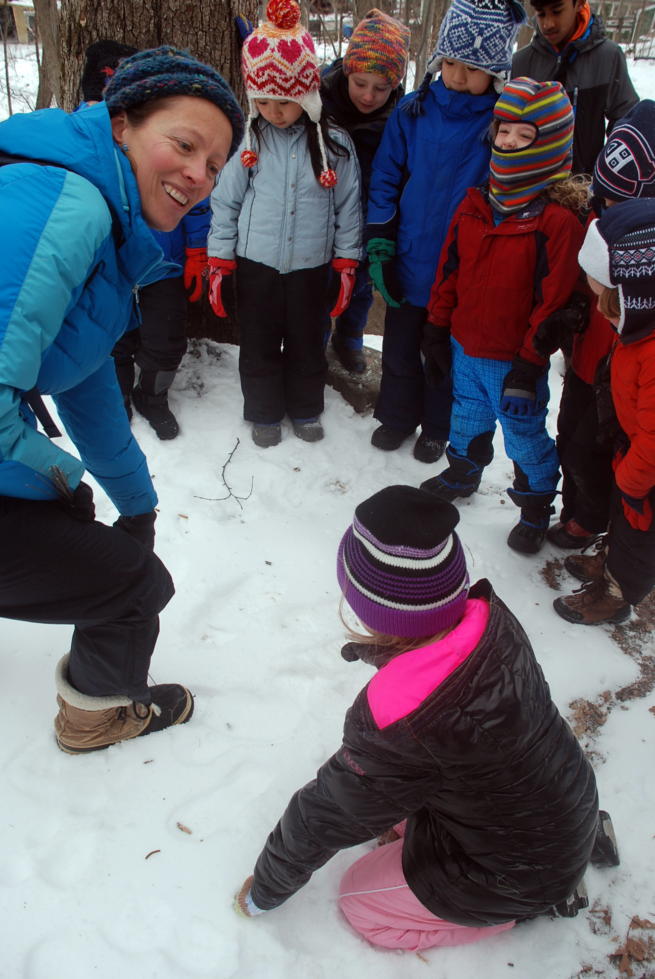 A group of young children and a teacher explore the woods and discover animal tracks in the snow.