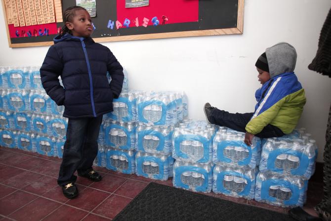 Justin Roberson (left), age 6, and Mychal Adams, age 1, wait on a stack of bottled water at a rally where the Rev. Jesse Jackson was speaking about about the water crisis in Flint, Michigan, Jan. 17, 2016. PHOTO: BILL PUGLIANO/GETTY IMAGES